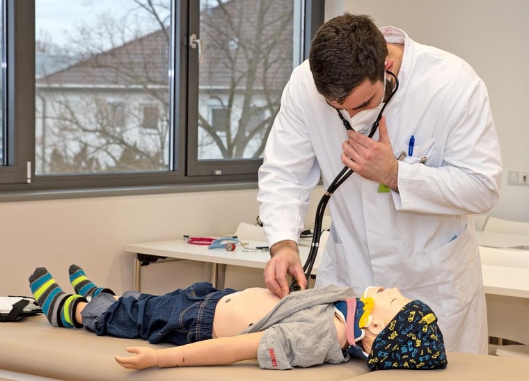 Ein Medizinstudent hört eine Kleinkind-Puppe bei den OSCE Prüfungen mit dem...